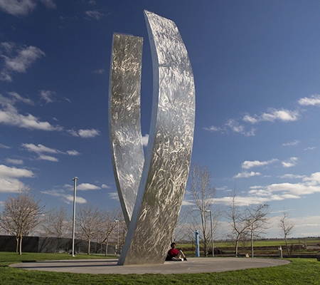 A lone campus community member leans against UC Merced's Beginnings sculpture.