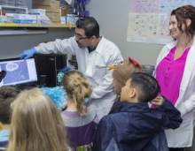 Two UC Merced faculty members show elementary students information on a computer.