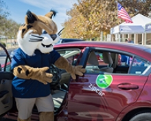 Campus mascot Rufus Bobcat stands next to one of new Zipcars in use at UC Merced.