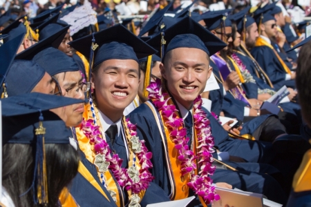 Students in blue caps and gowns smile at the camera during graduation.