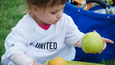 A toddler wearing a United Way shirt holds an apple.