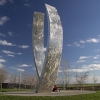 A lone campus community member leans against UC Merced's Beginnings sculpture.
